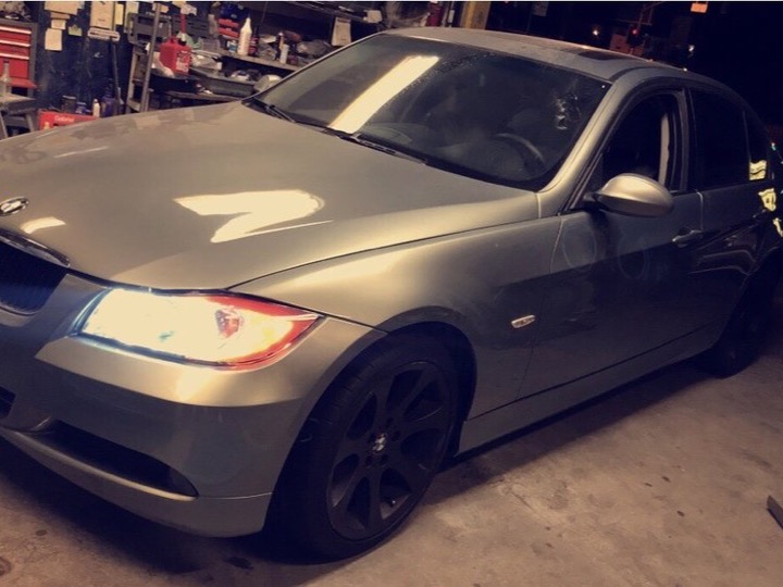 A silver BMW sedan parked inside the workshop at night, with a red tool chest, a workbench and a floor jack behind it.
