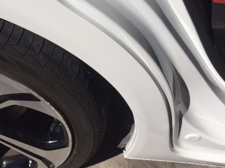 A white car body panel curving into the wheel arch, with the tire and wheel below it, in daylight.