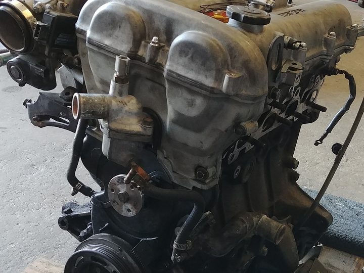 An engine out of a car, its cam covers and intake exposed, standing on the shop floor.